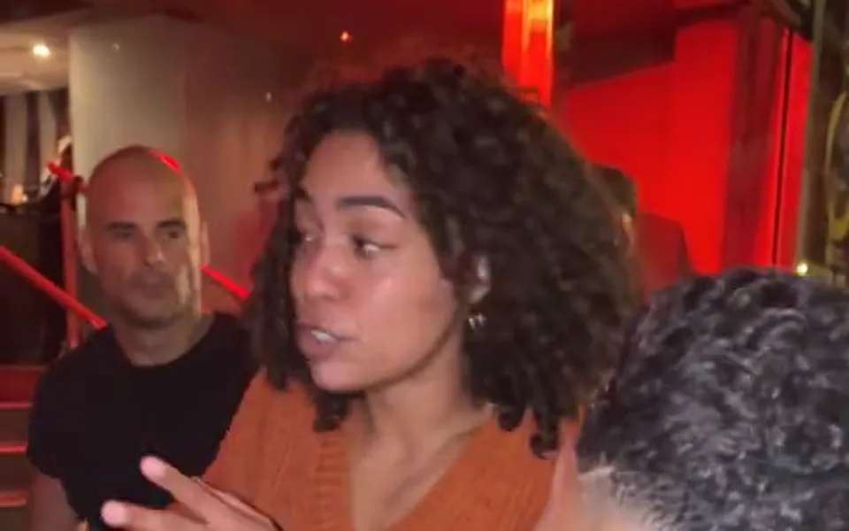 Frame from our Bulin 47 AI demo: she raps to the camera with an open hand while the man in front holds up a speaker and a phone.